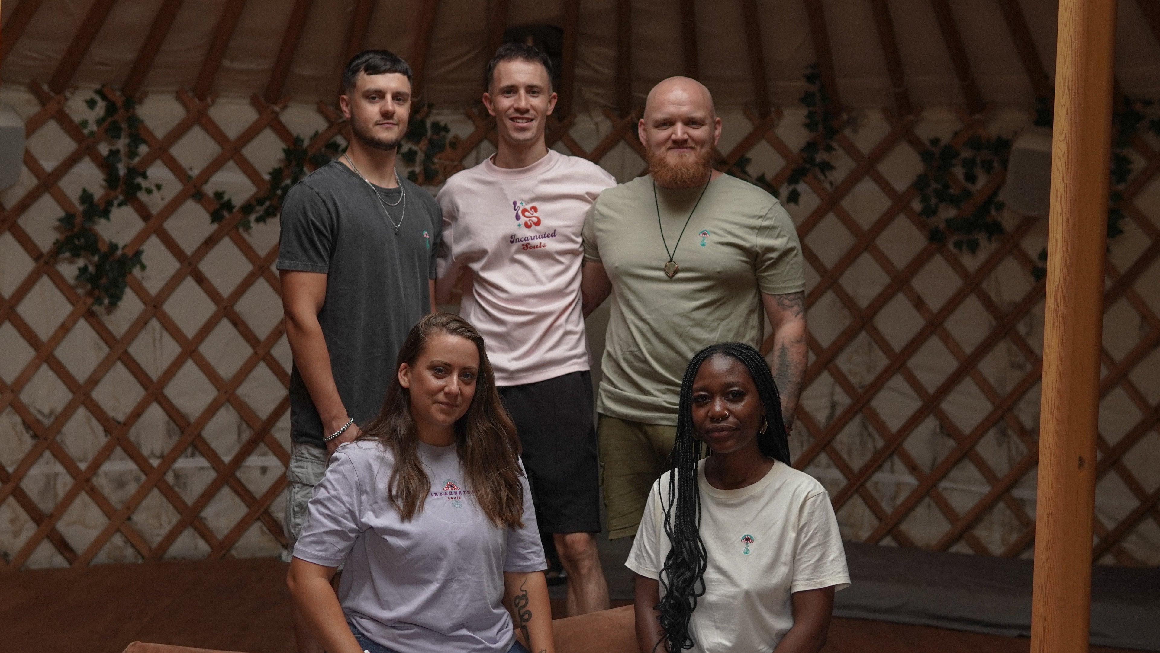 Group of five people posing inside a yurt with wooden walls.